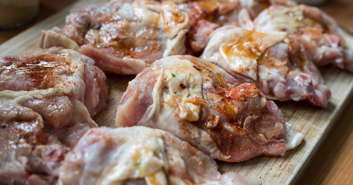 Raw chicken pieces seasoned with spices on a wooden board, ready for cooking.