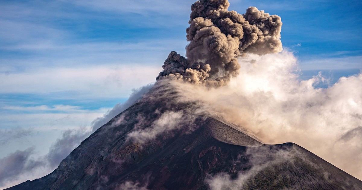 A breathtaking view of an erupting volcano with large plumes of smoke against a clear sky.