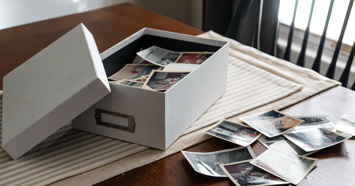 Open box of vintage family photos on wooden table by window.